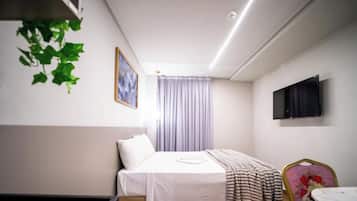 Ein Hotelzimmer mit einem Bett, einem Fernseher, einem Fenster mit Vorhängen und einer Pflanze.