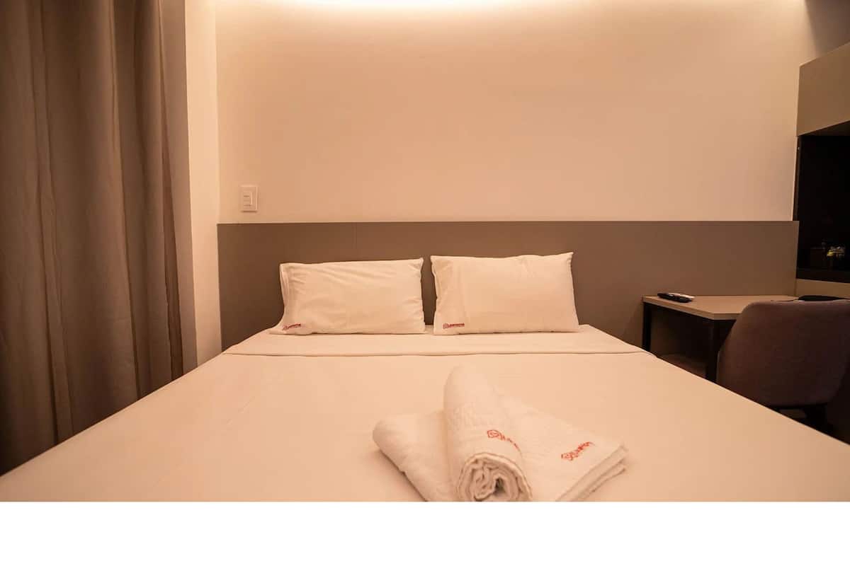 A hotel room with a bed, two pillows, a TV, and a chair.