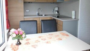A compact kitchen with wooden cabinets, a sink, a coffee maker, and a table with a floral tablecloth. - Holiday Villa in Sint Maartenszee (Sint Maartensvlotbrug)
