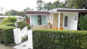 A single-story house with a white exterior, a brick chimney, and a small porch. - Holiday Villa in Sint Maartenszee (Sint Maartensvlotbrug)