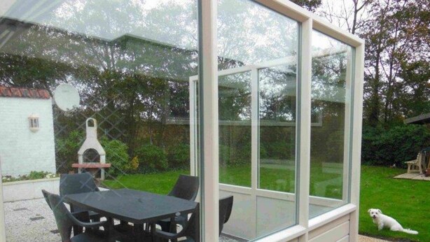 A conservatory with a table and chairs, a barbecue grill, and a dog in the garden. - Holiday Villa in Sint Maartenszee (Sint Maartensvlotbrug)