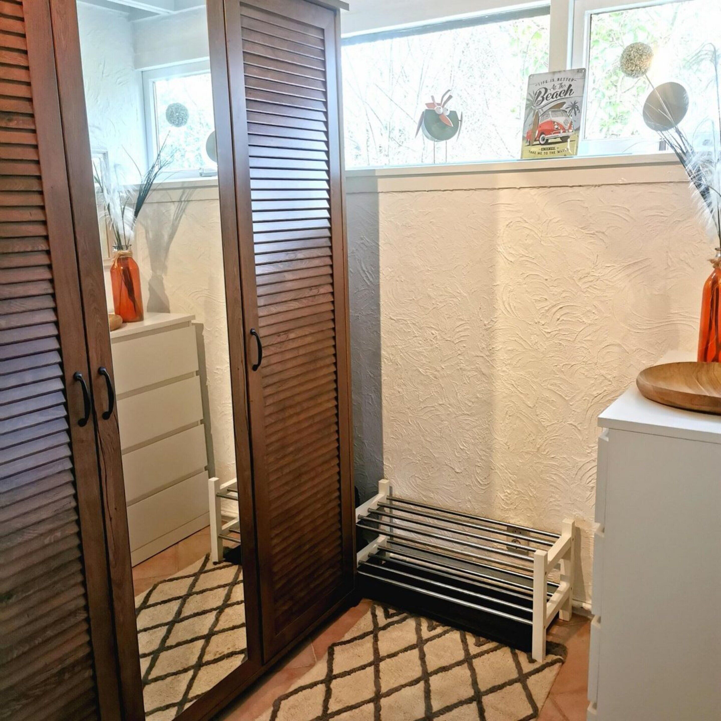 A room with a wooden wardrobe, a drying rack, and a small white cabinet.