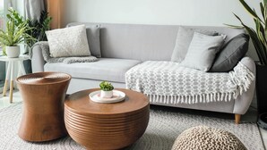 Ett modernt vardagsrum med en grå soffa, två inramade konstverk, ett runt soffbord i trä och en matta med struktur.