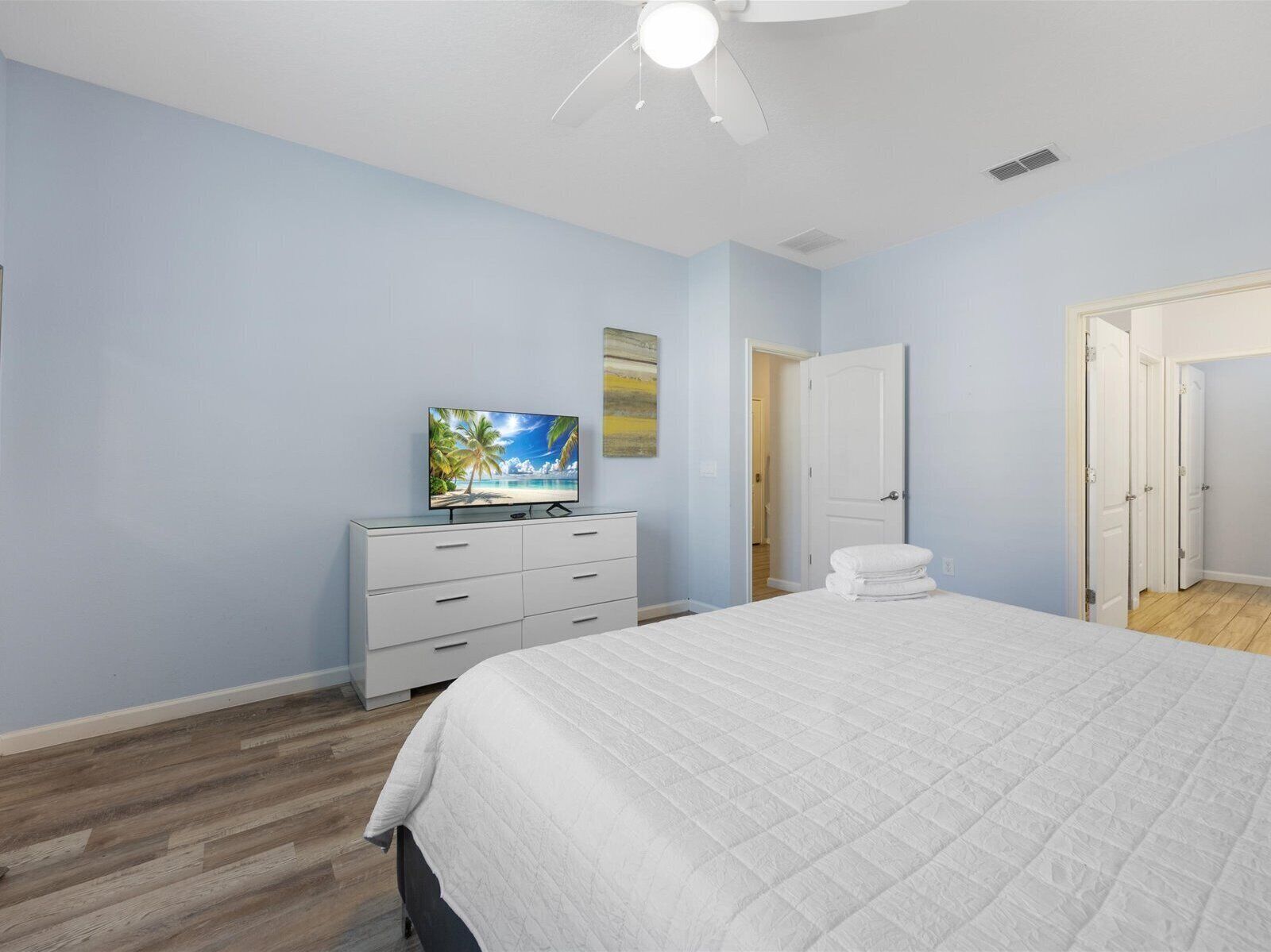 A bedroom with a bed, a TV on a dresser, and a door leading to another room.