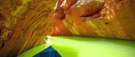 A boat in a cave with green water and red rock walls.