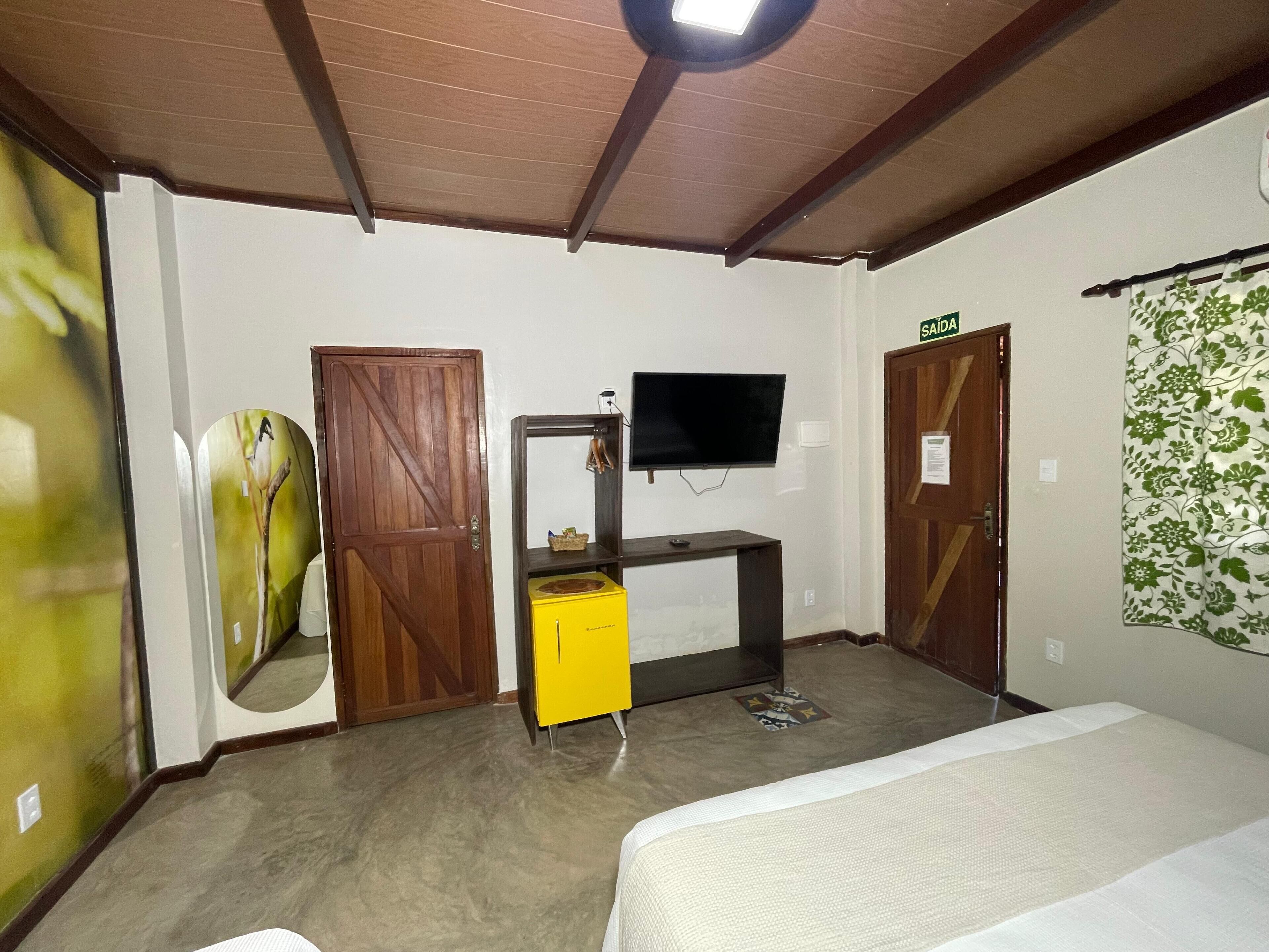 Una habitación con una cama, un televisor sobre un soporte, una puerta de madera y una cortina verde estampada en la pared.