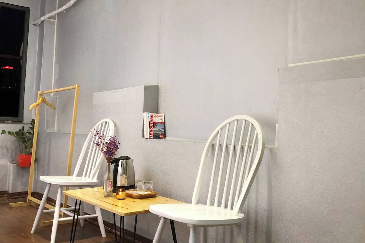 A room with two white chairs, a small wooden table, a kettle, and a potted plant.