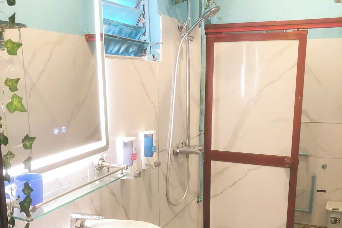 A bathroom with a glass shelf, a sink, a mirror, a shower, and a marble wall.