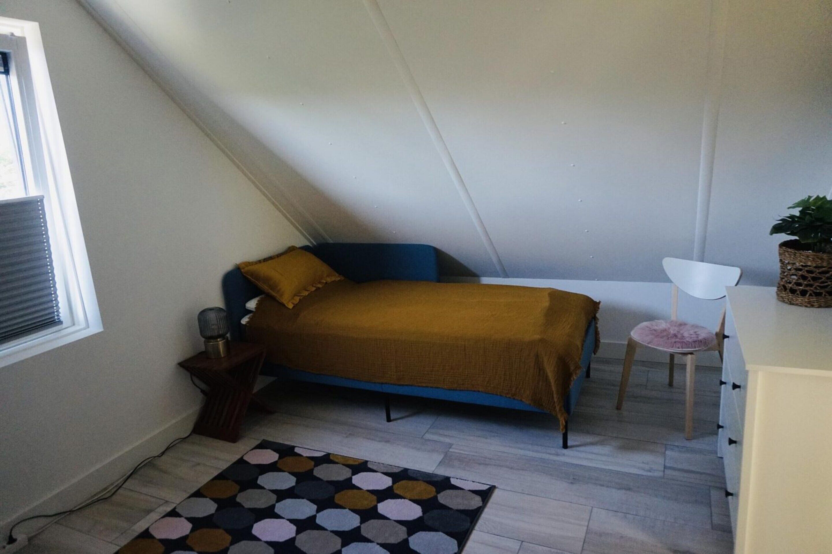 A small, cozy room with a bed, a chair, a small table, and a potted plant.