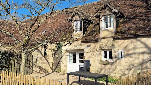 A rustic building with a wooden fence, a table, and chairs outside.