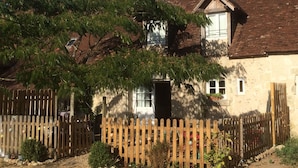 A rustic house with a wooden fence, a large tree, and a brick roof.