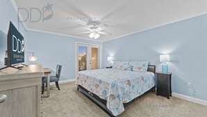 A bedroom with a bed, a desk, a chair, a nightstand, a lamp, and a ceiling fan.