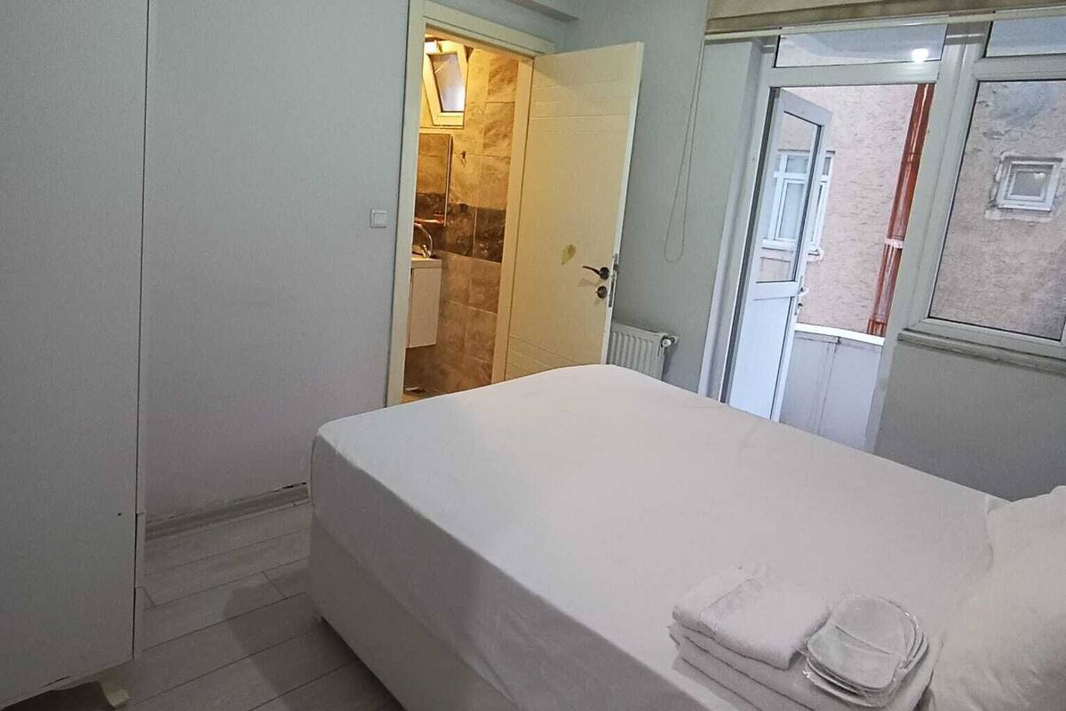 A bedroom with a bed, a door leading to a bathroom, and a window with a view of the outside.