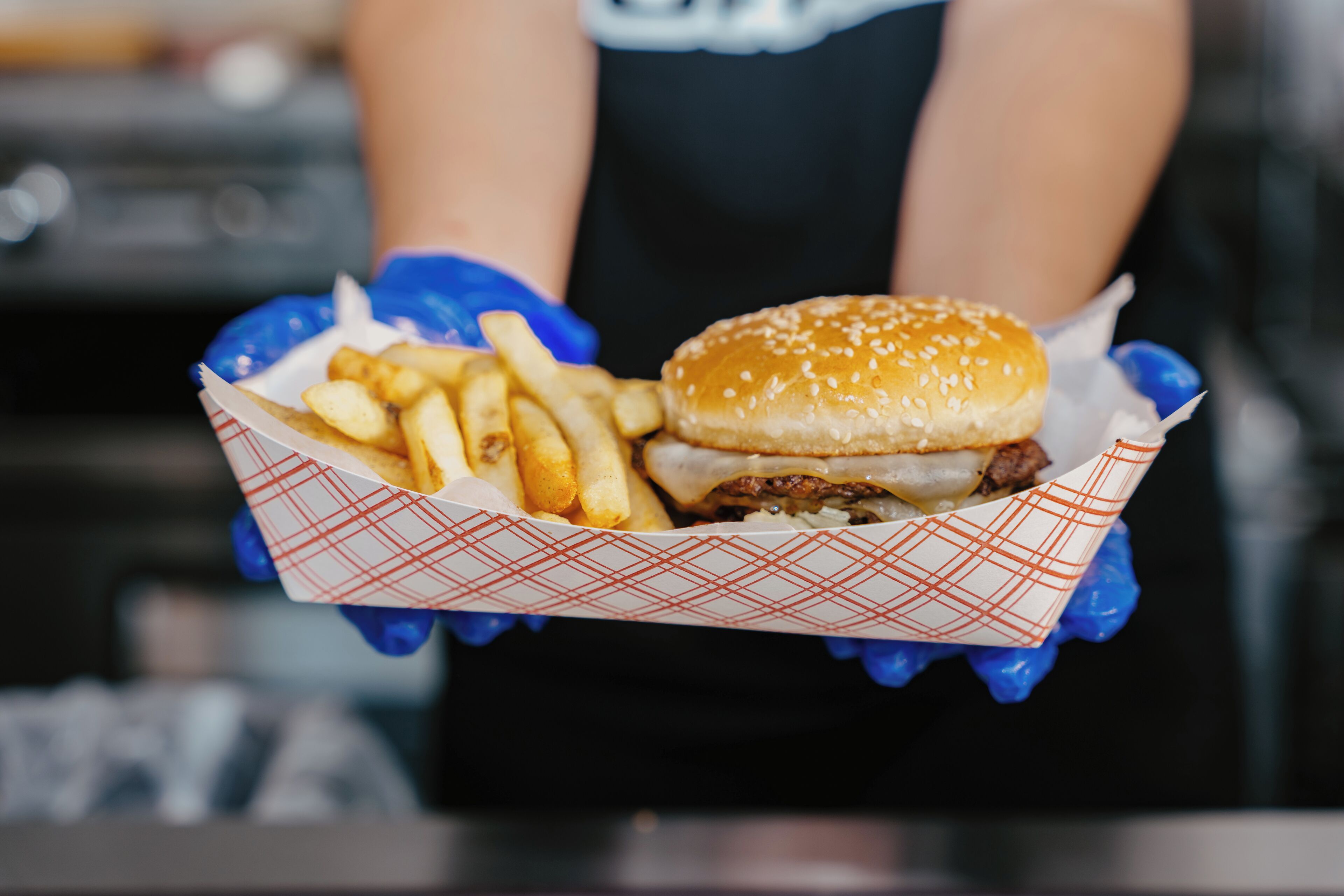 Una persona sosteniendo una bandeja de papel con una hamburguesa y papas fritas.