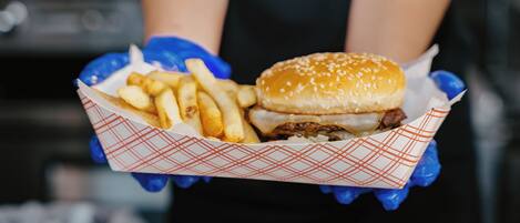 Una persona sosteniendo una bandeja de papel con una hamburguesa y papas fritas.
