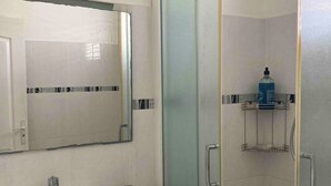 A bathroom with a white sink, a mirror, a shower with a glass door, and a shelf with toiletries. - Villa Soleil Located in a quiet, serene residential area (Vauclin)