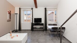 Ein modernes Wohnzimmer mit Flachbildfernseher, Esstisch mit Stühlen, weißem Sofa und Stehlampe.