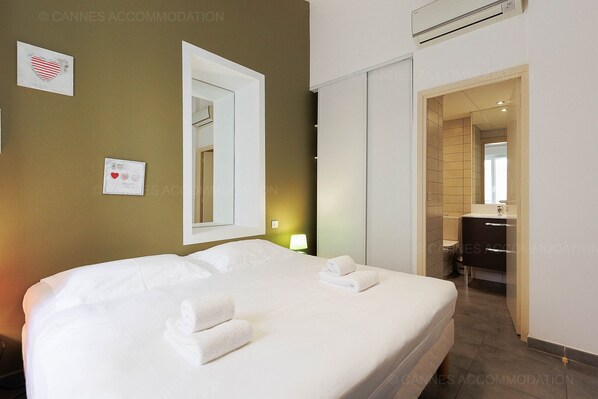 A hotel room with a large bed, a bedside table with a lamp, a mirror, and a bathroom visible through an open door.