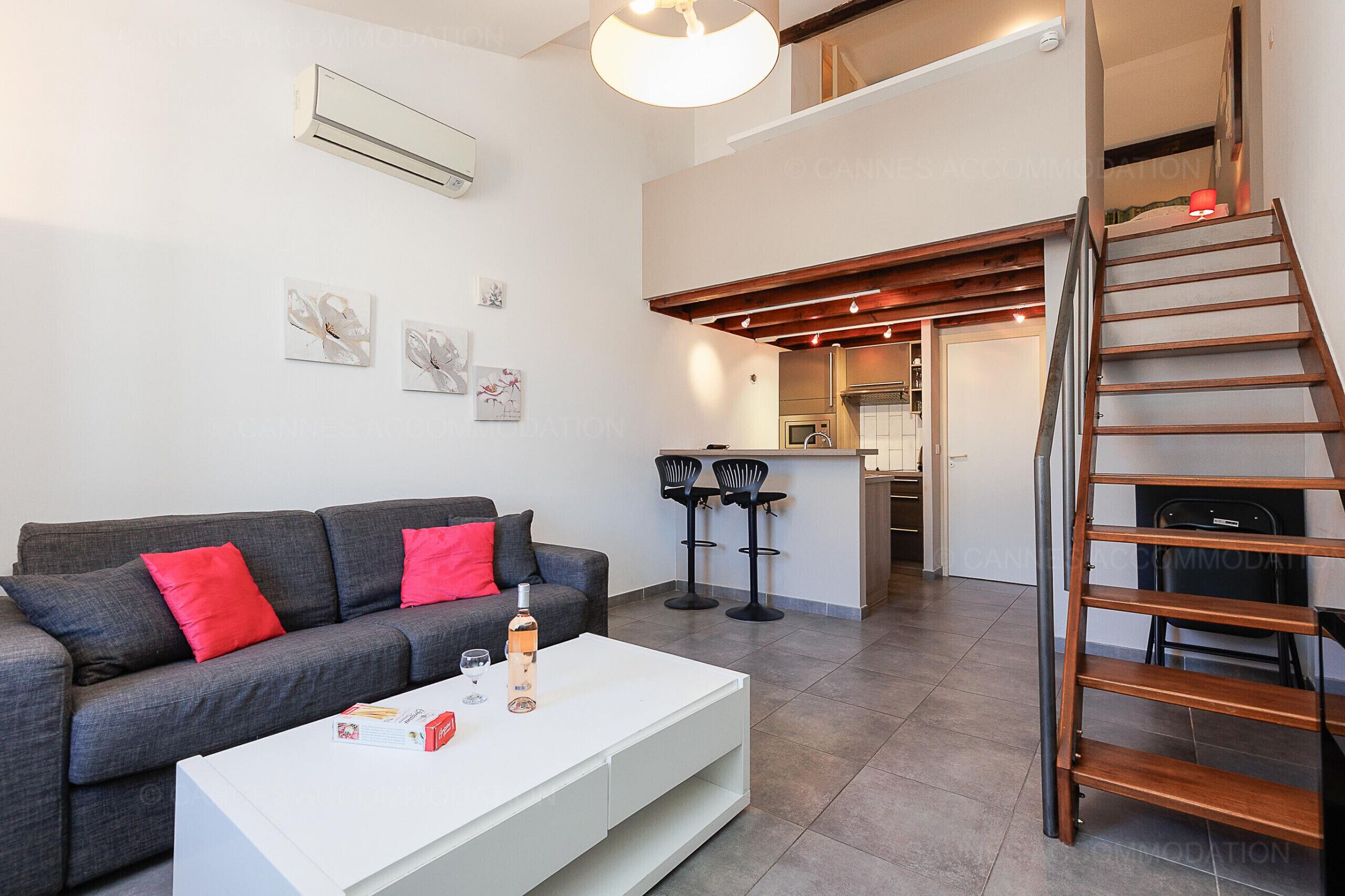 A modern living room with a grey sofa, red cushions, a white coffee table, and a staircase leading to an upper level.
