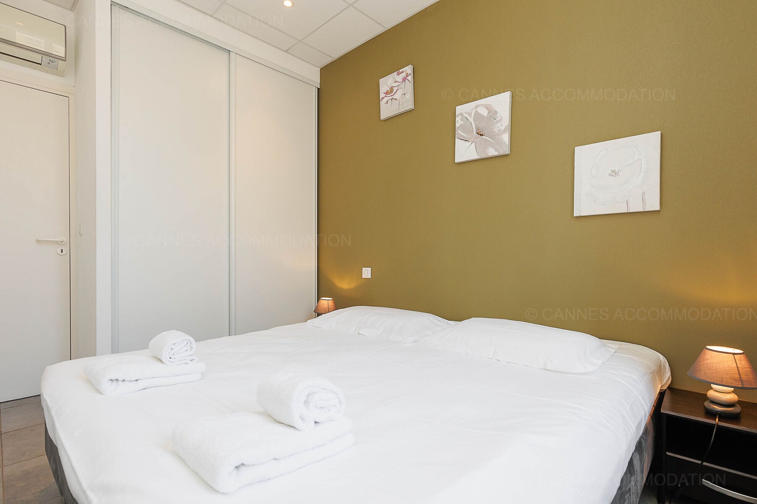 A neatly made bed with rolled towels, a bedside lamp, and artwork on the wall.