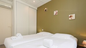 A hotel room with two beds, white linens, and towels. There are wall-mounted pictures and a bedside table with a lamp.