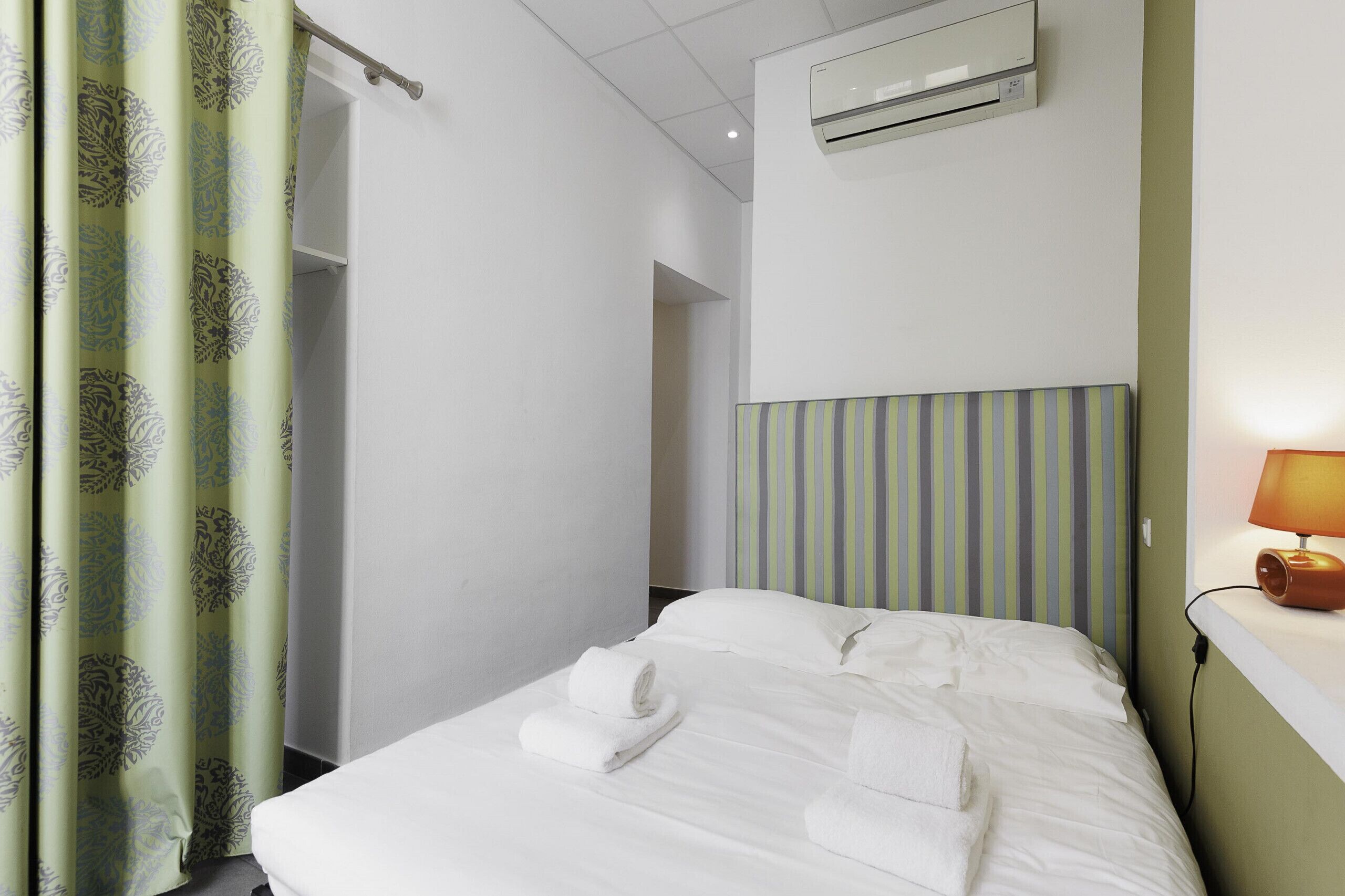 A hotel room with a bed, a bedside lamp, an air conditioner, and a striped headboard.
