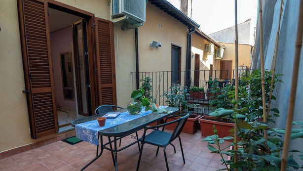 A patio with a table and chairs, surrounded by potted plants and a sliding door. - Room with terrace 1 (Tuscania)