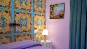 A bedroom with a patterned headboard, a painting on the wall, a bedside table with a lamp, and a purple bedspread. - Room with terrace 1 (Tuscania)