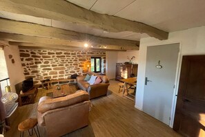 A cozy living room with a stone wall, leather sofas, a wooden dining table, and a door. - Cottage in Corrèze with Garden Views (LOUIGNAC)