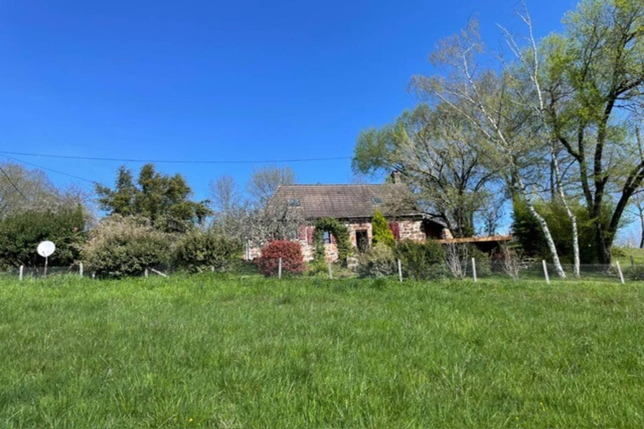 Una casa con fachada de piedra, rodeada por un campo cubierto de hierba y árboles.