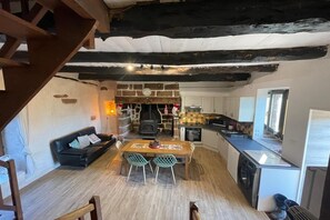 Eine gemütliche Küche mit Steinwand, Holzbalken, einer Essecke mit Tisch und Stühlen sowie einem schwarzen Ledersofa.