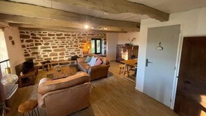 Un salon chaleureux avec des murs en pierre, des poutres en bois, un canapé, une table basse et un téléviseur.