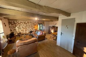 Tunnelmallinen olohuone, jossa on kiviseinät, puupalkit, sohva, sohvapöytä ja televisio.