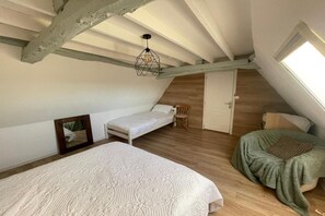 Ein Schlafzimmer mit schrägen Wänden, einem Bett, einem Sessel und einem Fenster.