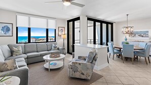 Una sala de estar moderna con un sofá gris, una mesa de centro redonda y un comedor con una isla blanca y sillas azules.