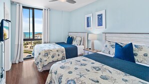Habitación de hotel con dos camas, ventilador de techo y vista al mar.