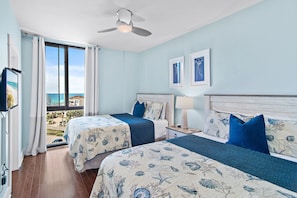 Habitación de hotel con dos camas, ventilador de techo y vista al mar.