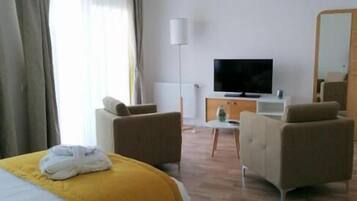 A hotel room with a bed, two armchairs, a TV, a lamp, and a mirror.