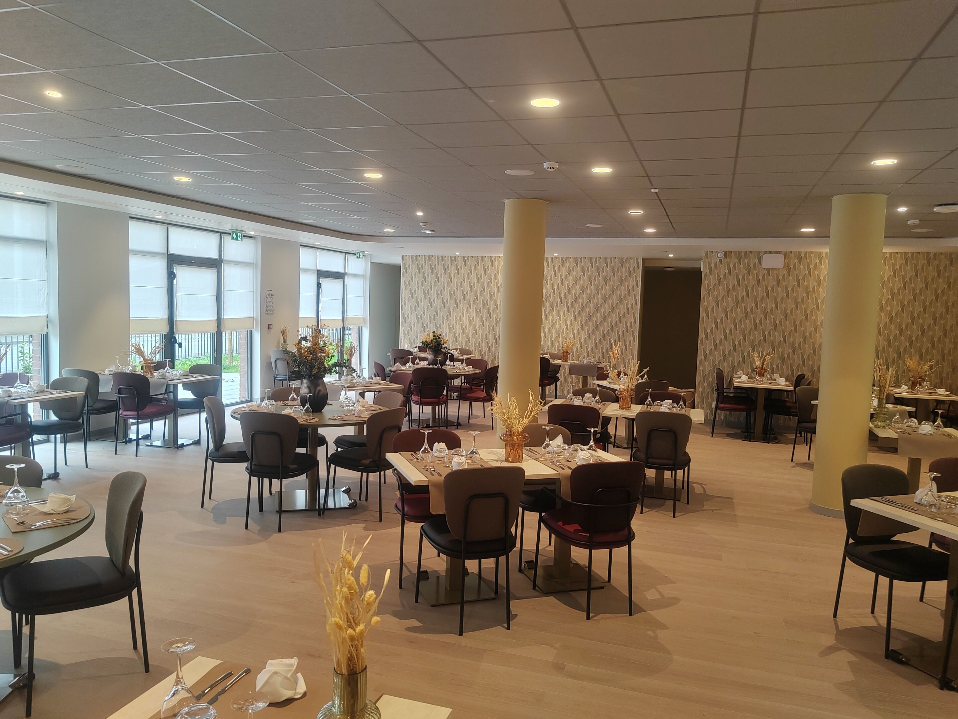 A spacious dining area with multiple tables and chairs, large windows, and decorative vases.