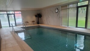 An indoor swimming pool with clear water, tiled walls, and a clock on the wall. - DOMITYS - La Flânerie (Béthune)