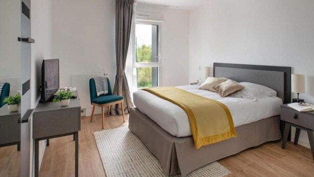 A modern bedroom with a bed, bedside table, chair, and a desk with a computer and plants. - DOMITYS - La Flânerie (Béthune)