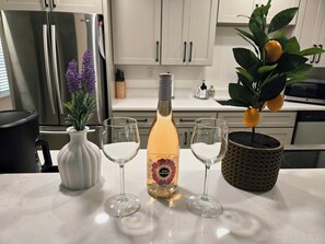 A kitchen counter with a bottle of rosé wine, two wine glasses, a potted plant with lemons, and a vase with purple flowers. - Charming New Smyrna Home Close to Shopping, Dining & Beach Fun! (New Smyrna Beach)