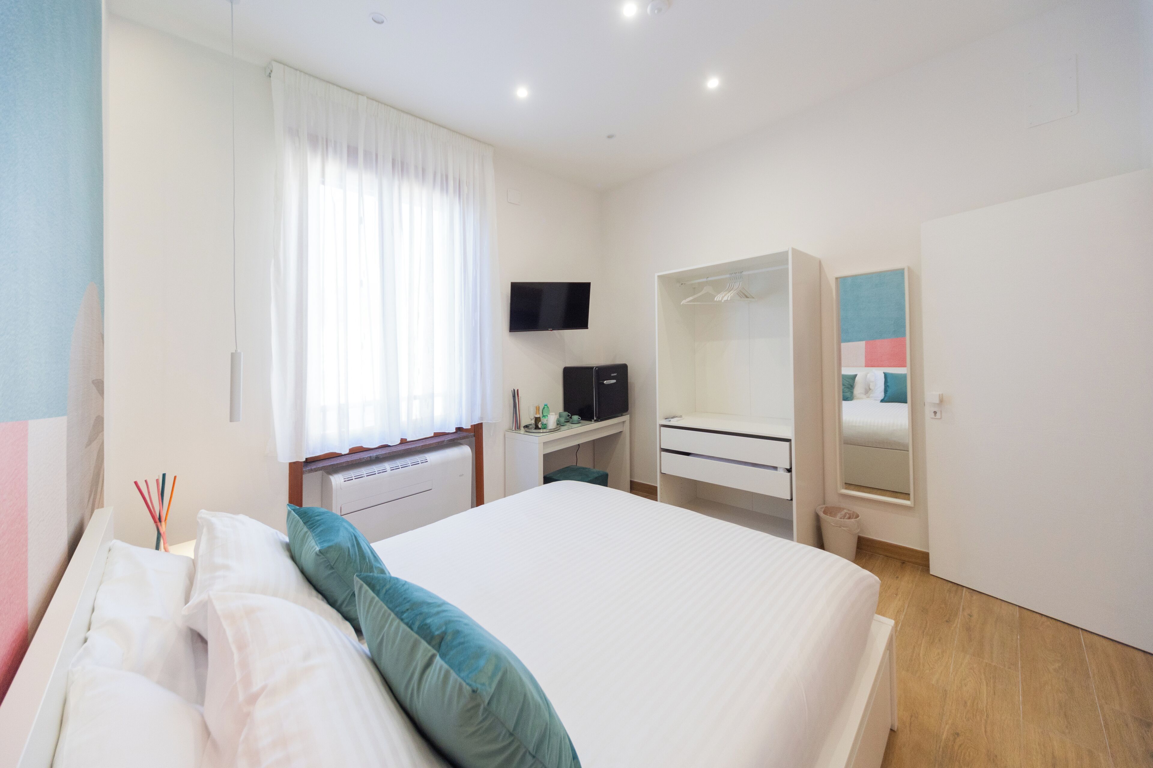 A bedroom with a bed, a desk, a TV, a wardrobe, and a mirror.