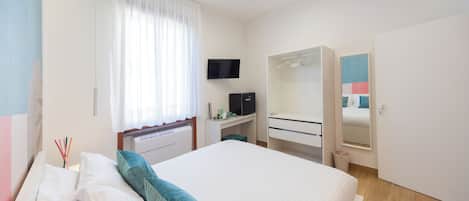 A bedroom with a bed, a desk, a TV, a wardrobe, and a mirror.