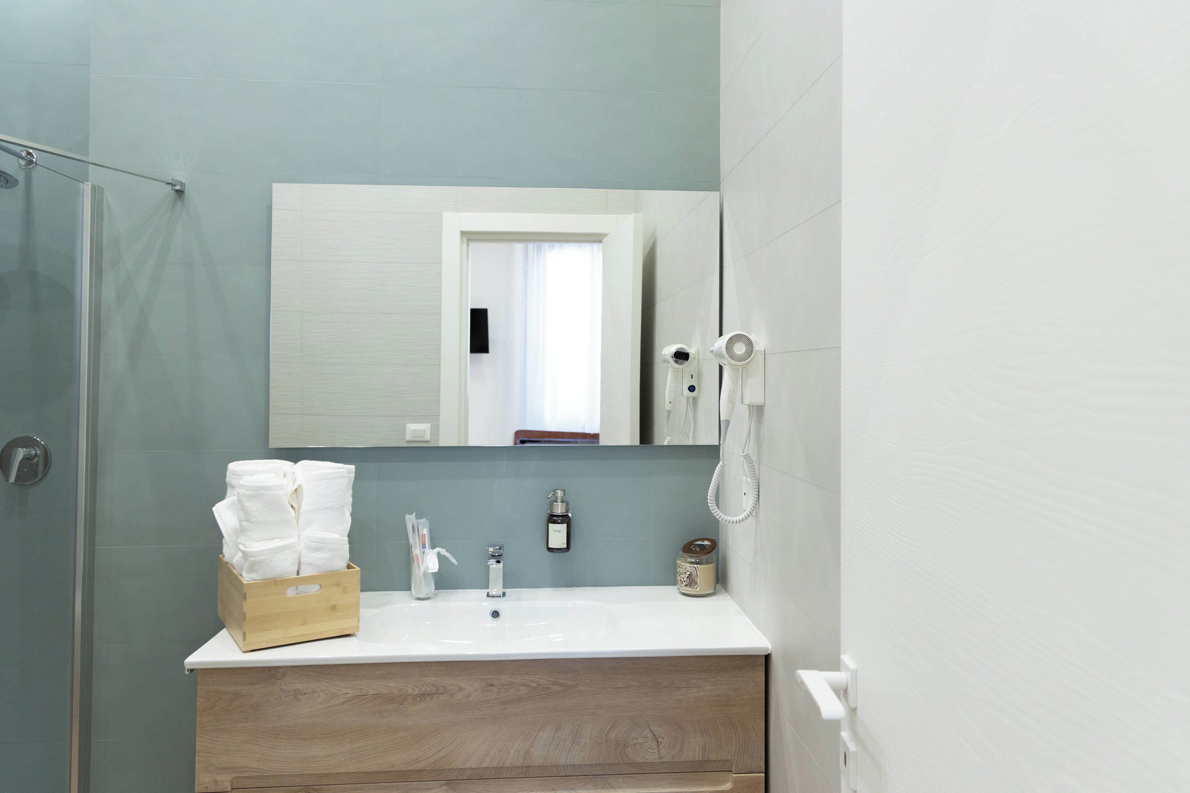 A bathroom with a wooden vanity, a white sink, a mirror, a glass shower enclosure, and a white toilet.