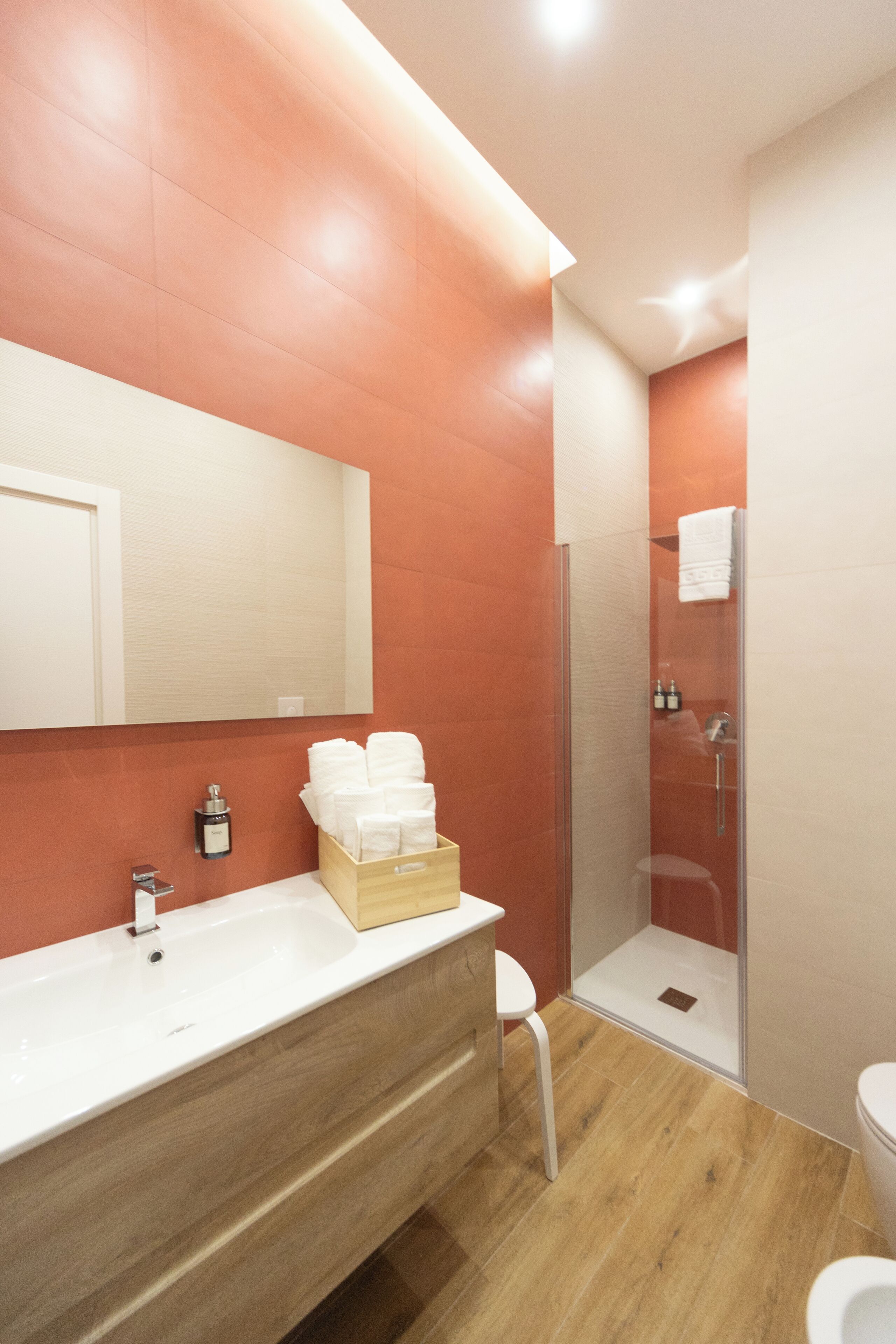 Un baño moderno con tocador de madera, cabina de ducha con vidrio y inodoro blanco.