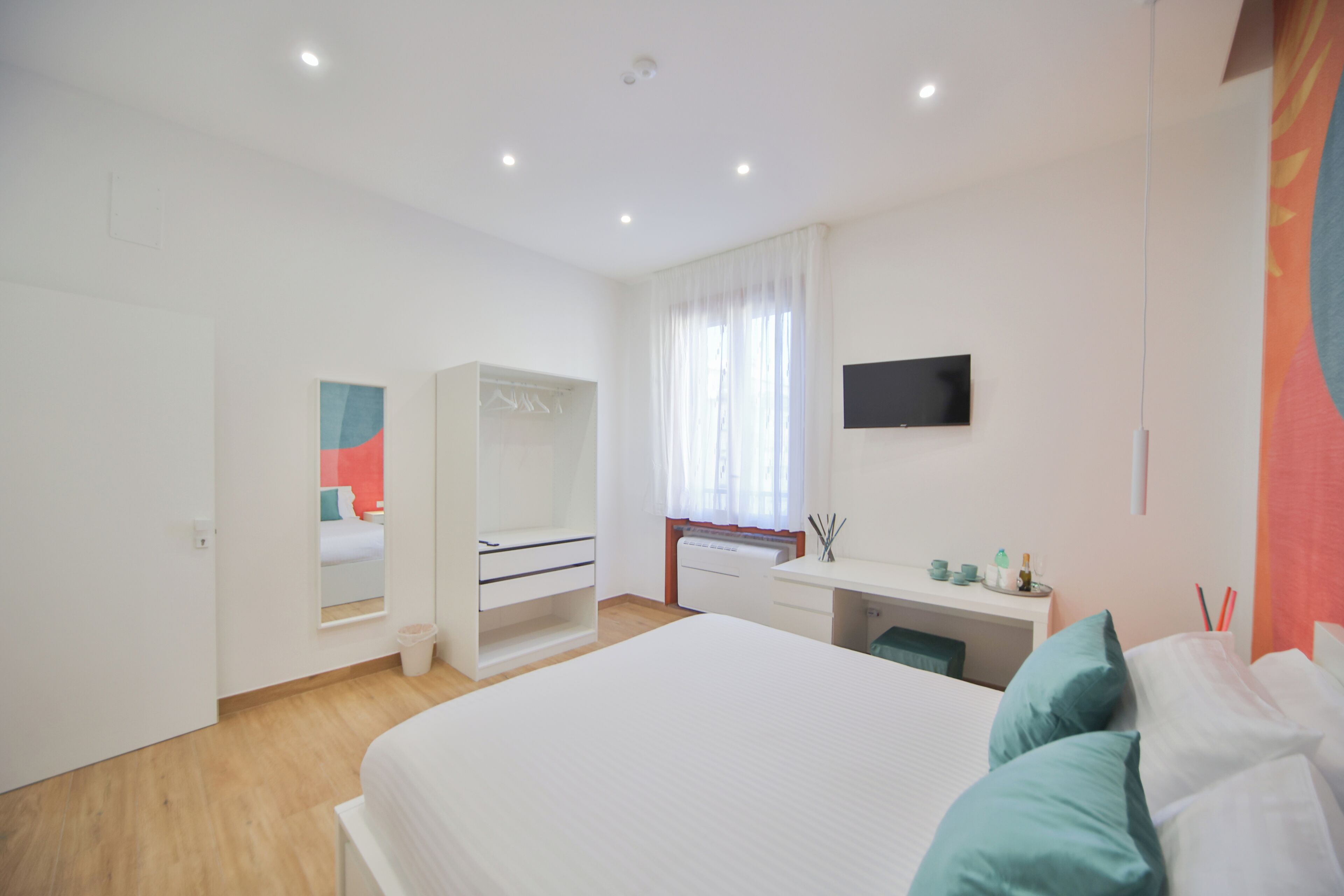 Une chambre moderne avec un grand lit, un dressing, un bureau et un téléviseur fixé au mur.