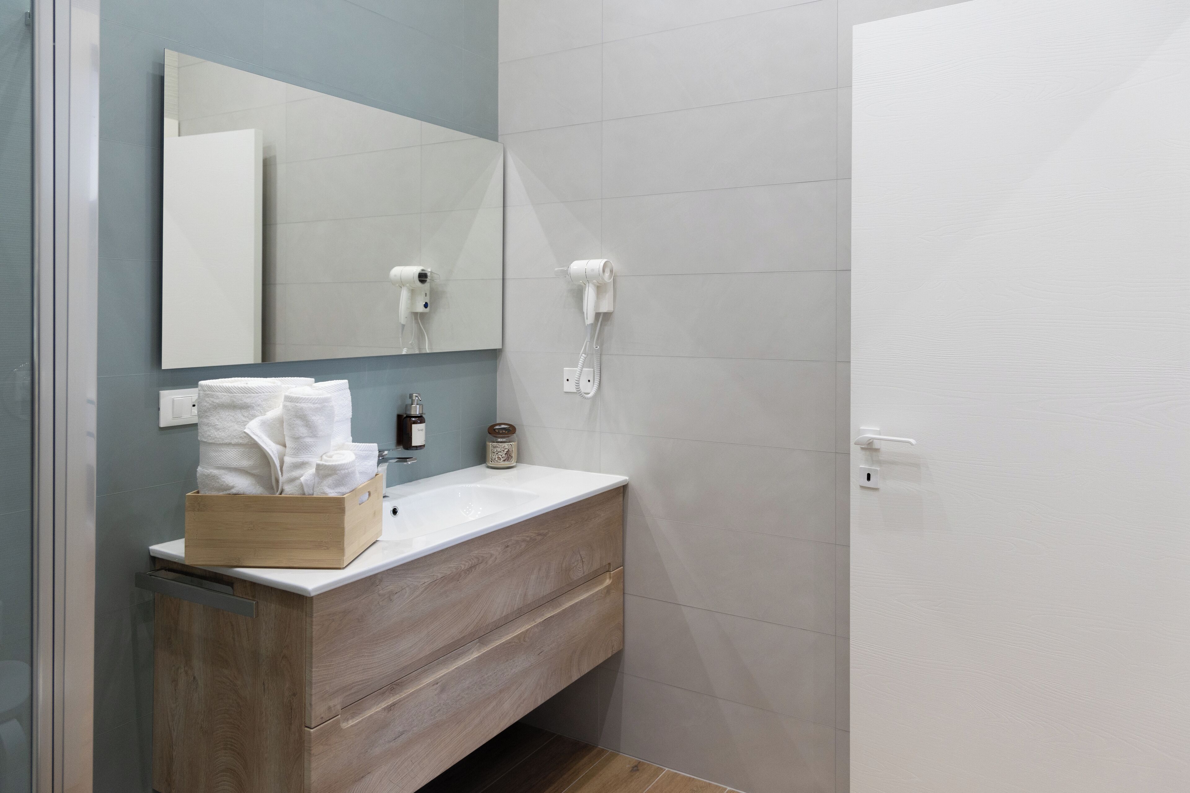 A modern bathroom with a wooden vanity, a large mirror, and two hair dryers mounted on the wall.