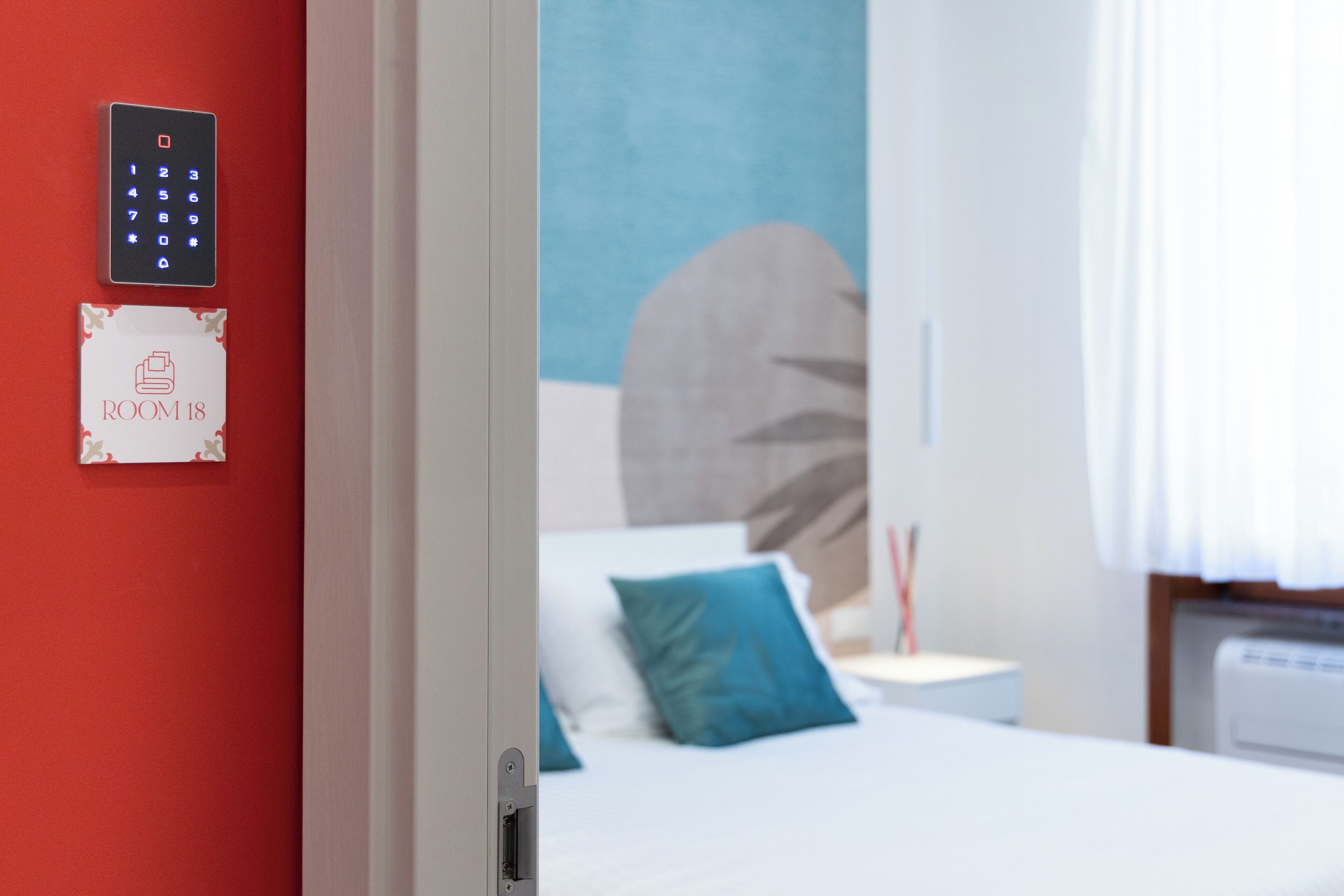 Habitación de hotel con pared roja, un teclado digital y un cartel que indica HABITACIÓN 18.