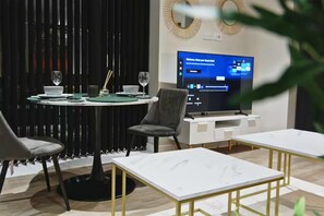Uma zona de refeições moderna com uma mesa redonda posta para dois, uma televisão de ecrã plano numa base e uma decoração minimalista.